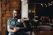 © mykolastock - Modern fashionable male student with beard, hat and eyeglasses reading book drinking coffee