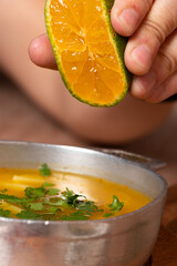 Wall Mural - Mano de persona exprimiendo un limon en una sopa de papa con cilantro y perejil. Plato de comida tradicional colombiana