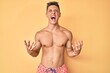 © Krakenimages.com - Young hispanic boy wearing swimwear shirtless crazy and mad shouting and yelling with aggressive expression and arms raised. frustration concept.