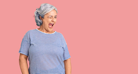 Senior woman with gray hair wearing casual striped clothes winking looking at the camera with sexy expression, cheerful and happy face.