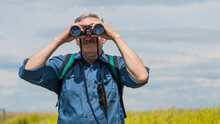 Man Looking Through Binoculars Searching For Wildlife On A Hike In A Beautiful Meadow Background	