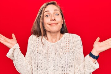 Young beautiful blonde woman wearing winter sweater over red isolated background clueless and confused with open arms, no idea and doubtful face.