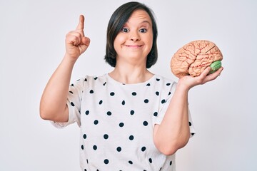 Brunette woman with down syndrome holding brain smiling with an idea or question pointing finger with happy face, number one