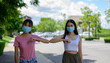 © PK Studio - Smiling young healthy mixed race female colleagues wearing facial medical masks greeting each other by bumping elbows gesture at workplace keeping social distance, preventing spreading covid19 virus