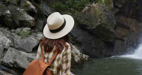 Canvas Print - Woman goes hiking and looks at the waterfall in forest