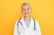 Isolated shot of confident experienced middle aged female doctor with short blonde haircut looking at camera with happy smile, wearing white medical coat and stethoscope around her neck