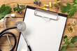 © kucherav - Alternative medicine. Clipboard with stethoscope, various plants, leaves of healing herbs, capsules and healthy oils on wooden table top view