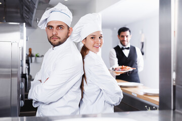 two confident fish restaurant chefs, standing back to back in kitchen