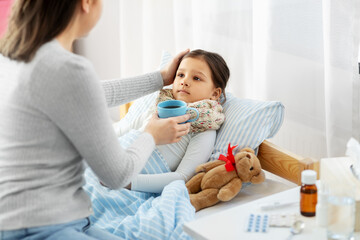 Sticker - family, health and people concept - mother giving mug with hot tea to sick little daughter lying in bed at home