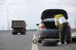 © alexkich - Replacing the wheel of a car on the road. A man doing tire work on the sidelines.