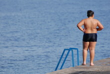 Overweight Obesity Concept Of One Little Thick Fat Boy In Swimming Shorts Standing On Beach During Summer Vacation