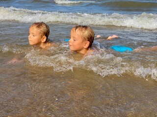 Wall Mural - Two twin boys splash in the waves in the sea on a sunny day. Valencia, Spain