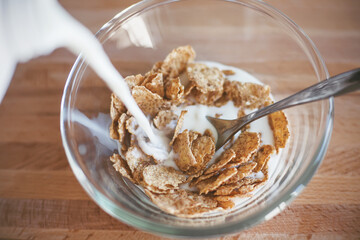 On a wooden table is a clear glass bowl with oatmeal cereals which is filled with milk. Delicious and light Breakfast in the early morning.