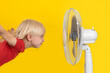 © somemeans - Blond boy with ventilator relaxing on yellow background. Summer heat