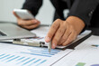 © PaeGAG - A businessman or accountant is sitting holding a pen to check the company's profit chart, the concept of growth planning in long-term investments.