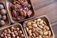 Different Nuts In Small Wooden Bowl On Dark Table. Row Of Bowls With Nuts, Top View. Peeled Nuts. Healthy Snack Concept