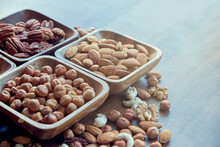 Different Nuts In Small Wooden Bowl On Dark Table. Row Of Bowls With Nuts, Top View. Peeled Nuts. Healthy Snack Concept