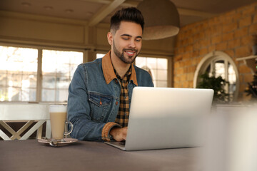 Wall Mural - Young blogger working with laptop at table in cafe