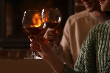 Canvas Print - Lovely couple with glasses of wine near fireplace indoors, closeup. Winter vacation