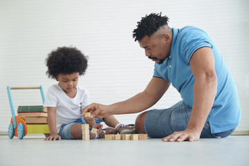 An African American family little son playing wooden blocks with father together on the floor at home