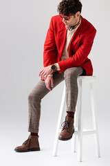 Wall Mural - trendy man in red blazer and sunglasses sitting on stool with bowed head on grey