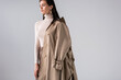 © LIGHTFIELD STUDIOS - attractive, trendy woman with trench coat on shoulder posing isolated on grey