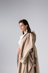 Wall Mural - beautiful, trendy woman with trench coat on shoulder posing isolated on grey