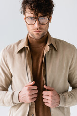 Wall Mural - serious, fashionable man in eyeglasses touching jacket isolated on grey