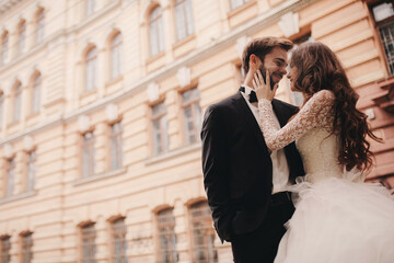 Happy newlywed couple hugging and kissing in old European town street, gorgeous bride in white wedding dress together with handsome groom. wedding day.