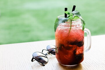 Closeup shot of a red drink with two straws near a glass on a wooden surface