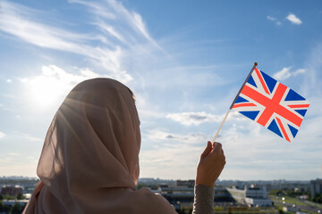 Silhouette of muslim woman in head scarf with Great Britain flag at blue sunset sky. Concept of freedom