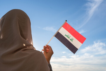 Wall Mural - Silhouette of muslim woman in head scarf with Iraq flag at blue sunset sky. Concept of freedom