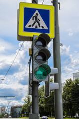 Traffic light with a burning green signal and a pedestrian crossing sign against the blue sky. Traffic safety, urban traffic regulation. Vertical image.