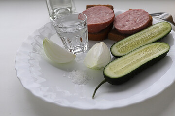 junk food on a white plate is a glass of vodka and a snack sandwiches with sausage