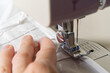 © Ilja - A woman works on a sewing machine. seamstress sews white curtains, close up view.