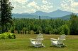 Inviting and restful scenic vista in Whitefield, New Hampshire. White lawn chairs overlooking hillside of lush evergreen trees framed by distant mountains in the White Mountains Presidential Range.