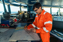 Filipino Deck Officer On Bridge Of Vessel Or Ship Wearing Coverall During Navigaton Watch At Sea . He Is Plotting Position On Chart
