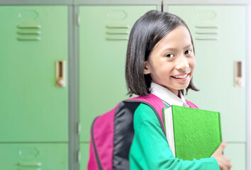 Asian little girl with book and backpack on the school