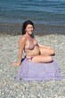 pregnant woman sitting and sunbathing on the beach,looking at camera