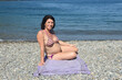 pregnant woman sitting and sunbathing on the beach,looking at camera