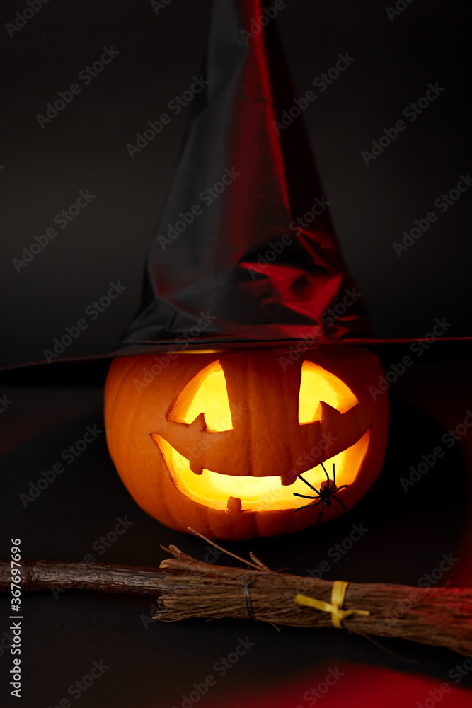 halloween and holiday decorations concept - jack-o-lantern in witch's hat with spider and broom in darkness - obrazy, fototapety, plakaty 