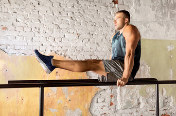 Wall Mural - fitness, sport, bodybuilding and people concept - young man doing abdominal exercise on parallel bars in gym