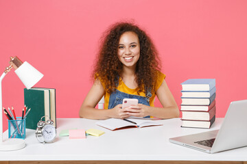 Canvas Print - Smiling african american girl employee in office sit isolated on pink background. Achievement business career. Education in school university college concept. Using mobile phone, typing sms message.