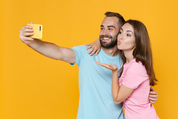 Wall Mural - Funny couple two friends guy girl in blue pink t-shirts isolated on yellow background. People lifestyle concept. Mock up copy space. Doing selfie shot on mobile phone hugging blowing sending air kiss.