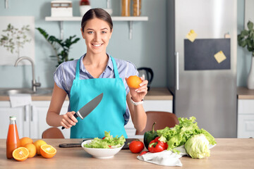 Beautiful young woman making vegetable salad in kitchen