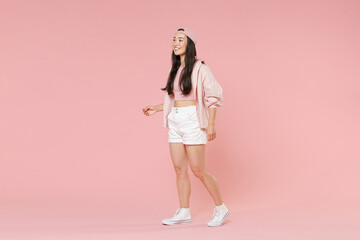 Wall Mural - Full length portrait of smiling young asian girl in casual clothes, cap isolated on pastel pink background studio portrait. People lifestyle concept. Mock up copy space. Walking going looking aside.