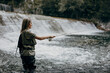 Young adult woman is fishing alone on fast mountain river. Active people and sport fly fishing concept.