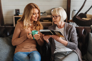 Senior mother and daughter looking photo book, resting at home