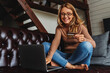 © InsideCreativeHouse - Smiling woman with credit card and laptop sitting on sofa at home. E-commerce concept