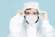 © zzzdim - Fully geared up doctor in a white costume covering all skin, wearing mask, gloves and glasses. Prepared for virus outbreak. Adjusting glasses, serious face expression.